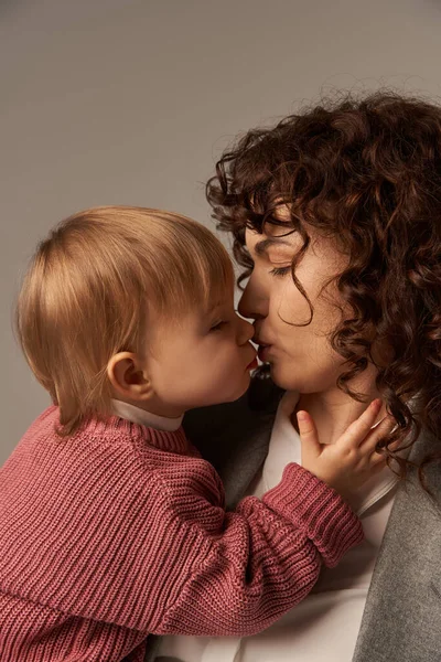 Малышка целует маму в костюме, сближается между матерью и дочерью, балансирует работу и жизнь, карьеру и семью, серый фон, любовь и нежность — стоковое фото