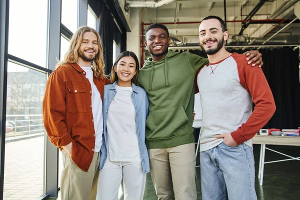 African american man embracing overjoyed interracial friends in stylish casual clothes looking at camera in modern office, diverse team business collaboration, startup project, entrepreneurship — Stock Photo