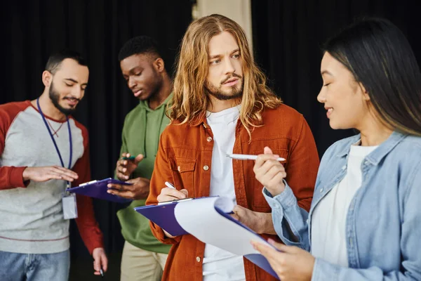 First aid training seminar, smiling asian woman with pen and clipboard talking to long haired man near paramedic and african american participant, safety and emergency preparedness concept — Stock Photo