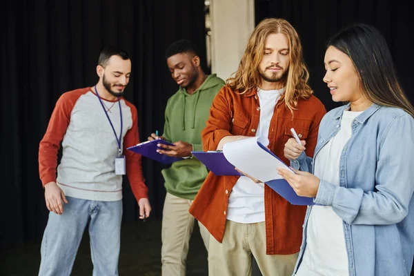 Medical seminar and first aid training, young asian woman with clipboard talking to long haired man near instructor and african american participant, safety and emergency response concept — Stock Photo