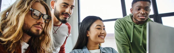 Inspirado multiétnico homens de negócios olhando para laptop perto overjoyed asiático mulher enquanto trabalhava em startup projeto no moderno escritório, colaboração de jovem criativo equipe, banner — Fotografia de Stock