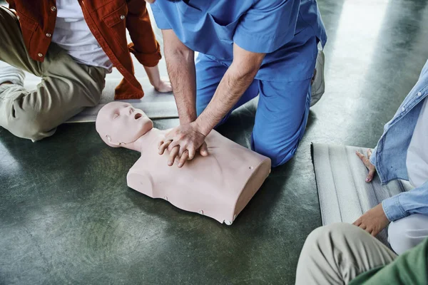 Erste Hilfe zum Anfassen, zugeschnittene Ansicht von Gesundheitshelfern, die Brustkompressionen an CPR-Schaufensterpuppen in der Nähe junger Teilnehmer durchführen, lebensrettende Fähigkeiten und Notfallvorsorgekonzept — Stockfoto