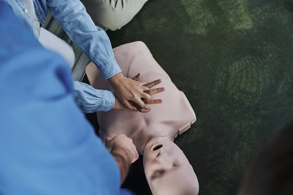 First aid seminar, top view of young woman practicing life-saving skills while doing chest compressions on CPR manikin near medical instructor, emergency situations response concept, cropped view — Stock Photo