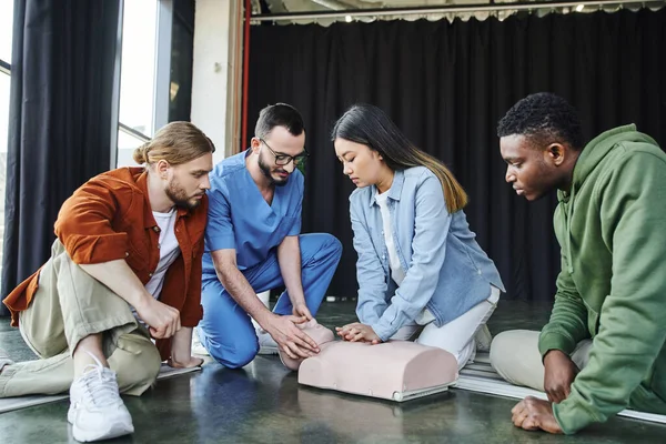 Medical seminar, first aid training, cardiopulmonary resuscitation, healthcare worker assisting asian woman practicing chest compressions on CPR manikin near multicultural participants — Stock Photo