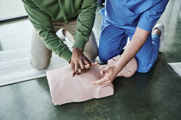 Cropped view of african american man practicing life-saving skills and doing chest compressions on CPR manikin near professional paramedic on first aid seminar, emergency preparedness concept, top view — Stock Photo
