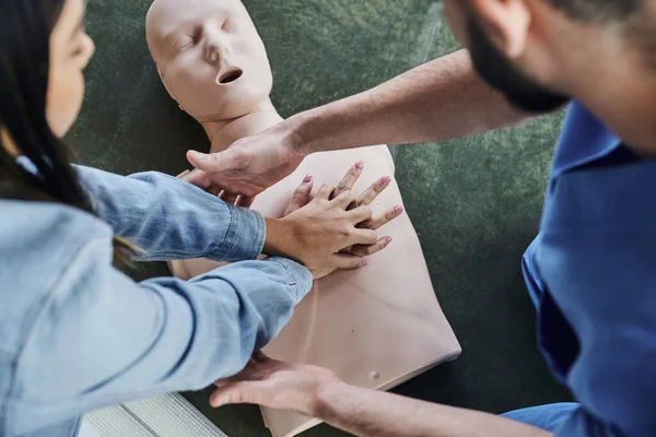 Ansicht von oben: junge Frau übt Brustkompressionen an CPR-Schaufensterpuppe während des praktischen Lernens auf einem Erste-Hilfe-Seminar in der Nähe eines medizinischen Instruktors, lebensrettende Fähigkeiten und Techniken — Stockfoto