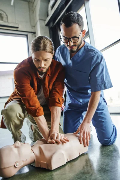 Erste-Hilfe-Kurse, professionelle Sanitäter, die jungen Mann beim Üben von Brustkompressionen an CPR-Schaufensterpuppen unterstützen, effektive lebensrettende Fähigkeiten und Notfallvorsorgekonzept — Stockfoto