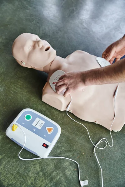 Обрізаний погляд на професійного медичного працівника, який застосовує дефібриляторні подушечки на CPR manikin, реанімацію серця, високий кут зору, охорону здоров'я та концепцію рятувальних методів — стокове фото