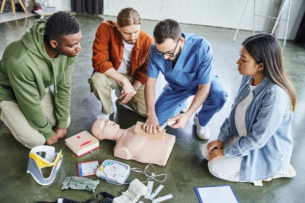 First aid seminar, high angle view of paramedic tamponing wound on simulator with bandage near multiethnic team and medical equipment, life-saving skills and emergency preparedness concept — Stock Photo