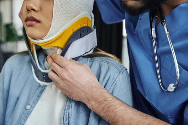 Vista recortada de instructor médico profesional con estetoscopio poner abrazadera del cuello en la mujer joven con la cabeza vendada, primeros auxilios y concepto de preparación para emergencias - foto de stock
