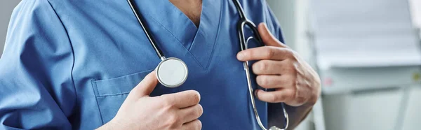 Ausgeschnittene Ansicht eines jungen Gesundheitshelfers in blauer Uniform, mit Stethoskop am Hals in der Klinik stehend, Erste-Hilfe-Seminar und Notfallkonzept, Banner — Stockfoto