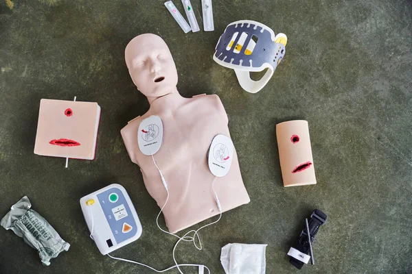 Top view of CPR manikin, automated external defibrillator, wound care simulators, neck brace, syringes, compression tourniquet and bandage, medical equipment for first aid training — Stock Photo