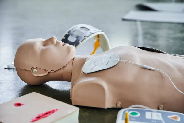 CPR manikin near automated external defibrillator, wound care simulator and neck brace on blurred background on floor in training room, medical equipment for first aid training — Stock Photo