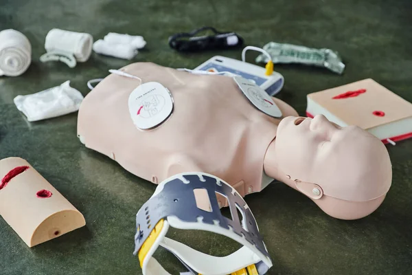 CPR training manikin near automated external defibrillator, wound care simulators, neck brace and bandages of floor in training room, medical equipment for first aid training and skills development — Stock Photo