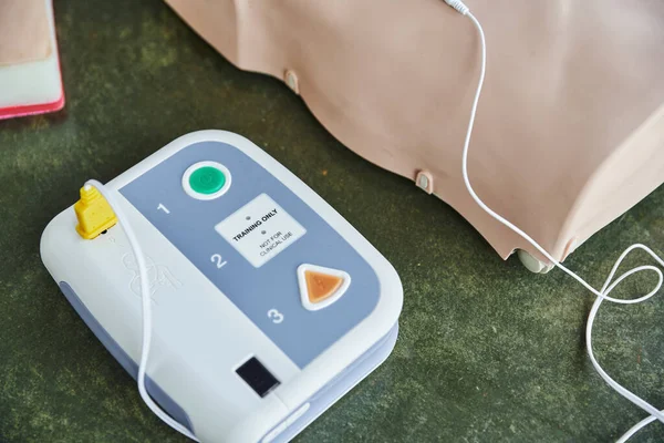 Hochwinkelaufnahme eines modernen automatisierten externen Defibrillators in der Nähe der CPR-Schaufensterpuppe im Schulungsraum, medizinisches Gerät für Erste-Hilfe-Schulungen und Kompetenzentwicklung — Stockfoto