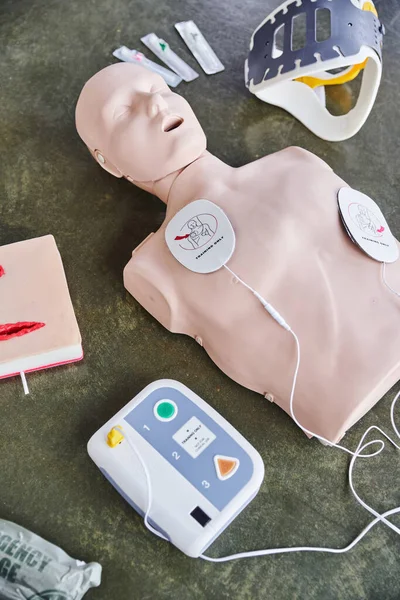 Vista de ángulo alto del maniquí de RCP, desfibrilador externo, simulador de cuidado de heridas, abrazadera para el cuello y jeringas en el suelo en la sala de entrenamiento, equipo médico para entrenamiento de primeros auxilios y desarrollo de habilidades - foto de stock