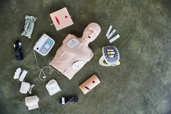 Vista dall'alto di manichino CPR, defibrillatore esterno automatizzato, simulatori di cura delle ferite, lancette emostatiche compressive, bende e siringhe, attrezzature mediche e concetto di primo soccorso — Foto stock
