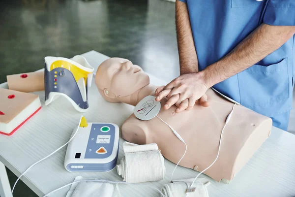 Cropped view of paramedic doing chest compressions on CPR manikin near defibrillator, compressive bandages and wound care simulators, emergency situations response concept — Stock Photo