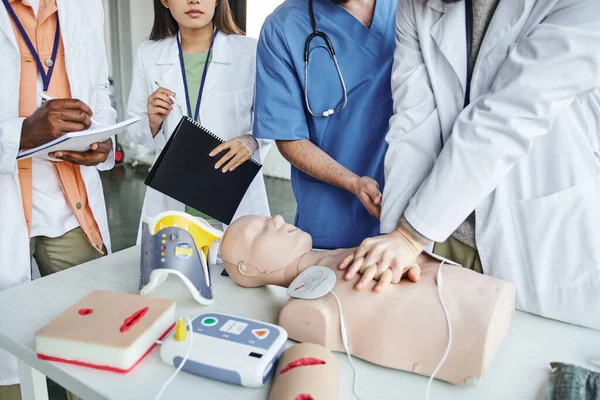 Cropped view of african american man writing in notebook next to healthcare worker doing chest compressions on CPR manikin  during first aid seminar, life-saving skills hands-on learning concept — Stock Photo