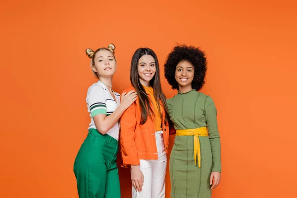 Group of interracial teenage models in stylish outfit posing and smiling at camera while standing together on orange background, trendy generation z concept, friendship and companionship — Stock Photo