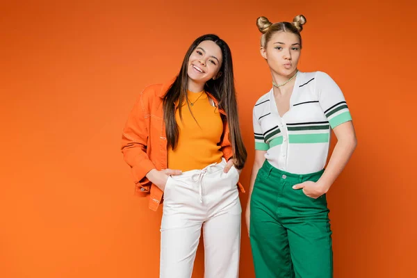Confident and cheerful teenage girlfriends in casual outfits posing and pouting lips while looking at camera on orange background, fashionable girls with sense of style, friendship and bonding — Stock Photo
