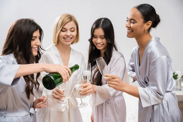Весільний душ, жінка наливає шампанське в окуляри поблизу міжрасових подруг, святкування, наречена і подружки нареченої, брюнетка і блондинка, різноманітність, весільний душ, кращі друзі, чотири жінки, святкові — стокове фото