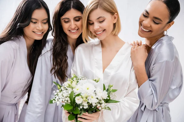 Brautschau, vier Frauen, glückliche Braut mit Blumenstrauß in der Nähe von Brautjungfern in Seidenroben, kulturelle Vielfalt, Spaß zusammen, Freundschaftsziele, brünette und blonde Frauen, Lächeln und Freude — Stockfoto