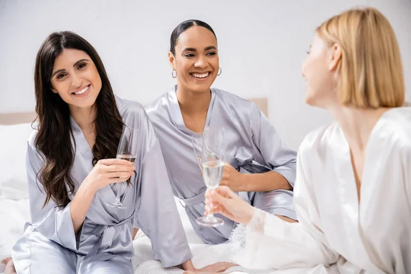 Bridal party, wedding prep, interracial girlfriends holding glasses with champagne, celebration, brunette and blonde women, bride and her bridesmaids, cultural diversity, excitement, bedroom — Stock Photo