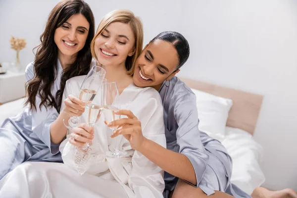 Bridal shower, multicultural girlfriends clinking glasses with champagne, celebration, brunette and blonde women, bride and her bridesmaids, cultural diversity, excitement, bedroom — Stock Photo