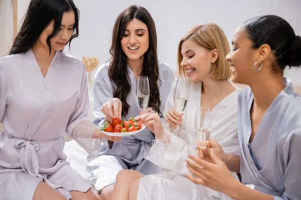 Strawberries and champagne, four women, bridal party, interracial girlfriends having fun, brunette and blonde, bride and her bridesmaids spending time together, cultural diversity, bedroom — Stock Photo