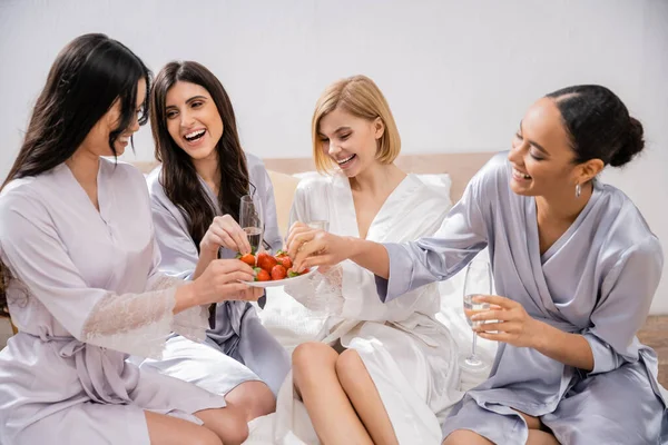 Strawberries and champagne, happy four women, bridal party, interracial girlfriends having fun, brunette and blonde, bride and her bridesmaids spending time together, cultural diversity, bedroom — Stock Photo