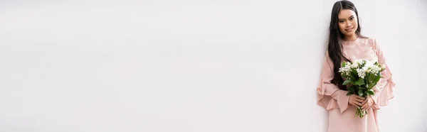 Damigella d'onore asiatica in abito rosa pastello con bouquet, donna felice con capelli castani su sfondo grigio, fiori bianchi, occasione speciale, matrimonio, moda, sorriso e gioia, banner — Foto stock
