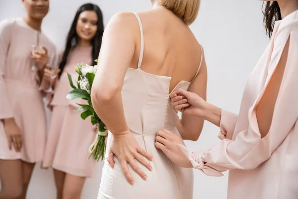 Preparações de casamento, dama de honra zipping vestido de noiva loira, mulheres inter-raciais no fundo cinza borrado, diversidade racial, moda, morena e mulheres loiras, buquê de noiva — Fotografia de Stock