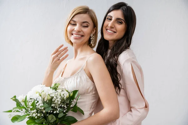 Special occasion, bridesmaid hugging bride, showing engagement ring, friendship goals, grey background, happy girlfriends, bridal bouquet, blonde and brunette women, white flowers, happiness — Stock Photo