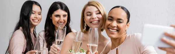 Four women, beautiful bride and her interracial bridesmaids taking selfie together, happiness, champagne glasses, bridal bouquet, wedding dress, bridesmaid gown, brunette and blonde women, banner — Stock Photo