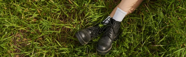 Вид зверху на ноги жінки в стильних чоботях, що сидять на трав'янистих лугах на відкритому повітрі, природний пейзаж — стокове фото