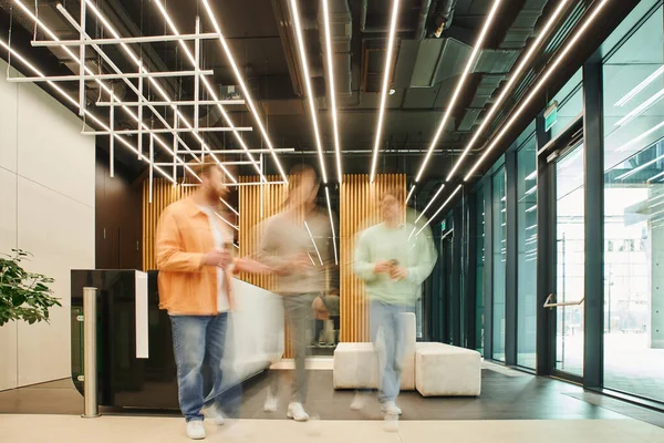 Long exposure of businessmen with takeaway drinks walking and talking in lobby of modern coworking office with high tech interior, discussing and planning startup project during coffee break — Stock Photo