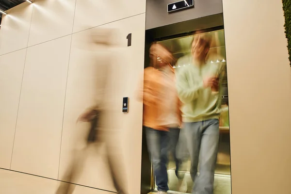 Desenfoque de movimiento de los empresarios energéticos que salen de ascensor en la oficina contemporánea de coworking, larga exposición, movimiento, colaboración, negocio dinámico y concepto de productividad - foto de stock