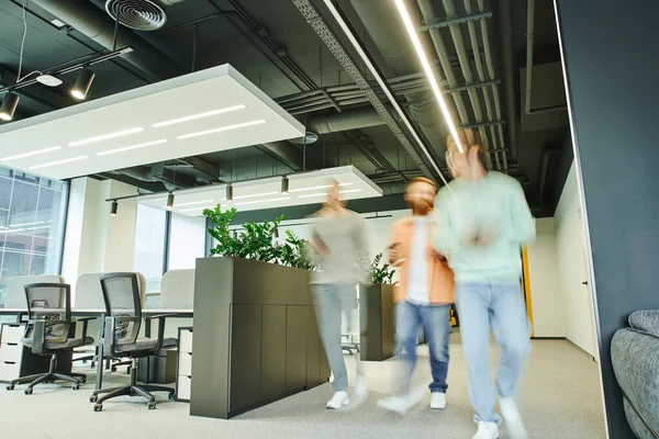 Equipo de emprendedores enérgicos caminando a lo largo del espacio de coworking contemporáneo con interior de alta tecnología, muebles de oficina y plantas naturales verdes, movimiento, larga exposición, negocio dinámico - foto de stock
