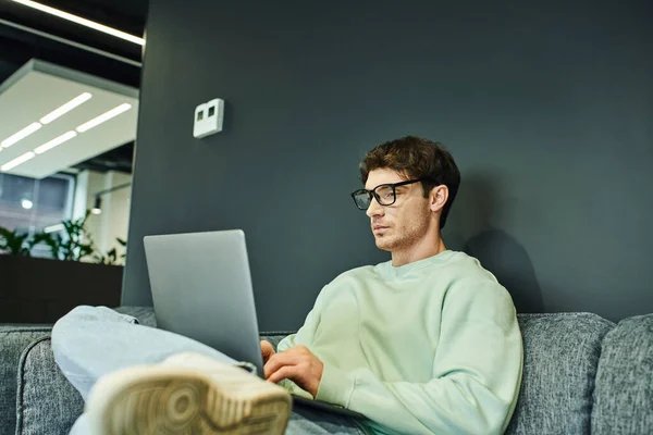 Empreendedor sério em óculos elegantes e projeto de inicialização de planejamento de roupas casuais no laptop no escritório de co-trabalho moderno, concentração e produtividade, estilo de vida empresarial — Fotografia de Stock