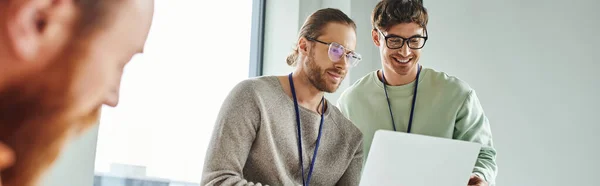 Creative architects in casual clothes and eyeglasses looking at laptop near colleague working on blurred foreground, collaboration, innovative ideas, modern coworking office, banner — Stock Photo