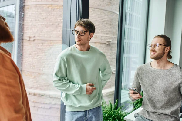 Positive entrepreneurs in eyeglasses and stylish casual clothes looking away through window in contemporary office while planning new startup project, concept of successful collaboration — Stock Photo