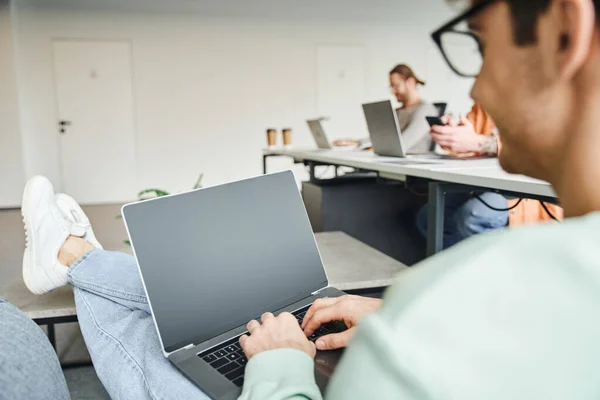 Geschäftsmann tippt auf Laptop mit leerem Bildschirm, während er im modernen Coworking-Büro an einem Startup-Projekt arbeitet, auf verschwommenem Vordergrund, erfolgreiches Unternehmertum-Konzept — Stockfoto