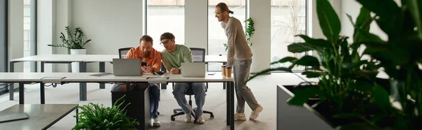 Entrepreneur in casual clothes standing next to colleagues working on new business project near computers in modern office environment with high tech interior and natural plants, banner — Stock Photo