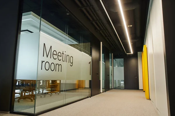 Конференц-зал за прозрачной стеклянной стеной, длинный и широкий коридор с освещением в современном коворкинг-офисе с высокотехнологичным интерьером, концепцией организации рабочего пространства — стоковое фото