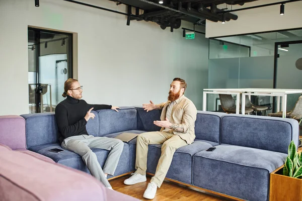 Stylish business colleagues discussing startup project and gesturing while sitting on soft couch in modern lounge of coworking office, partnership and success concept — Stock Photo