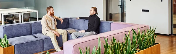 Imprenditori eleganti e ambiziosi seduti su un divano morbido e progettano un progetto di startup vicino a piante verdi in salotto di uffici moderni, partnership e concetto di successo, banner — Foto stock