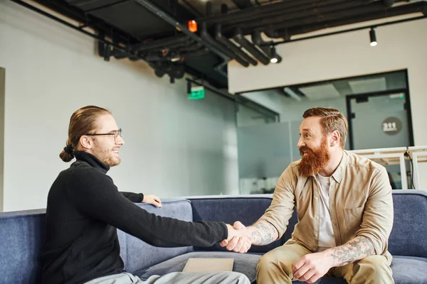 Pleased business partners shaking hands and smiling at each other while confirming agreement in lounge of modern office environment, partnership and success concept — Stock Photo