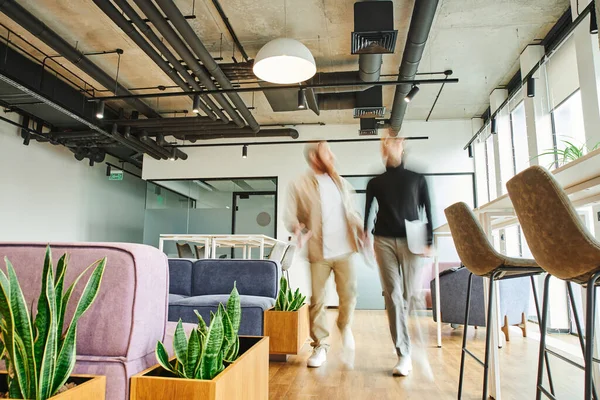 Motion blur of entrepreneur with laptop walking next to business partner and discussing startup in office lounge with high tech interior, modern furniture, natural plants, dynamic business concept — Stock Photo