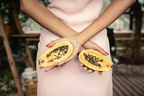 Ausgeschnittene Ansicht einer jungen afrikanisch-amerikanischen Frau im Sommerkleid, die frische Papaya in der Hand hält und im verschwommenen Innengarten steht, trendige Frau umgeben von tropischer Üppigkeit — Stockfoto